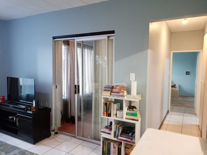 A living room area featuring tiled flooring and a sliding glass door leading to an adjacent space, with an open archway to the hallway.