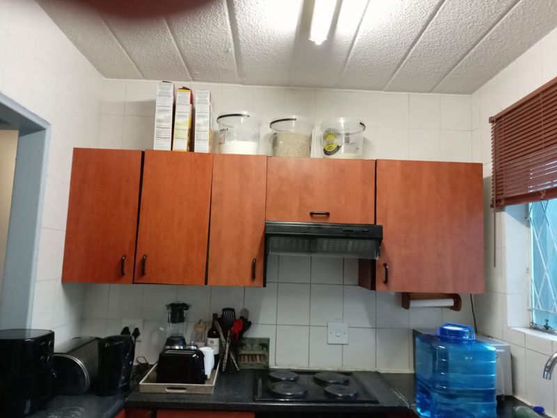 A functional kitchen area featuring wood-finish cabinetry, a built-in electric hob with extractor fan, and tiled splashback walls.