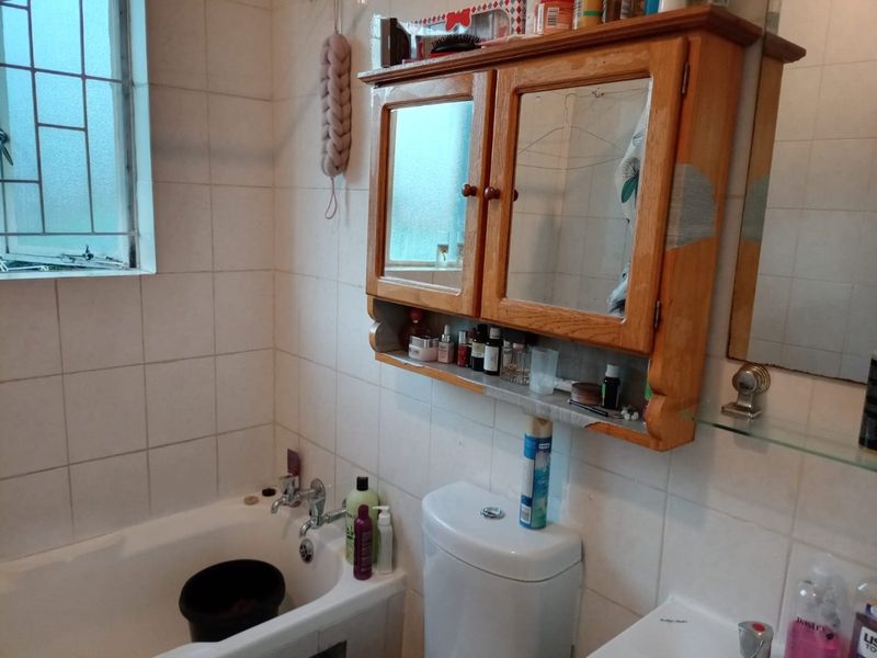 A functional bathroom featuring a bathtub, toilet, and wall-mounted wooden medicine cabinet with tiled wall finishes.