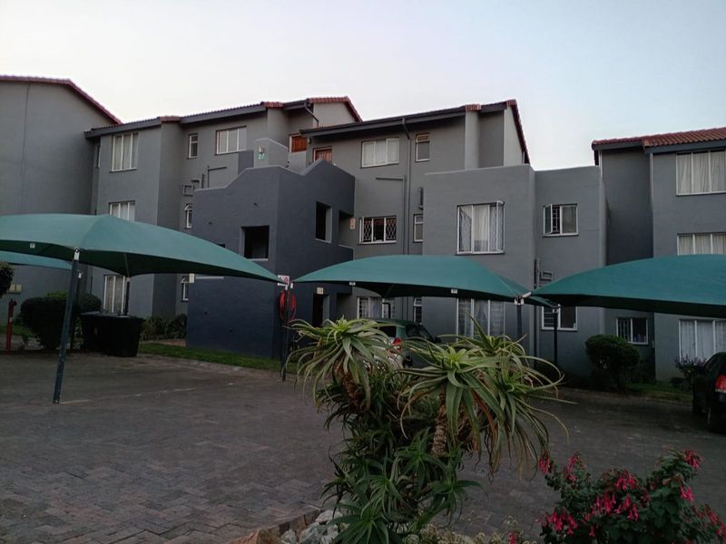 Exterior view of a multi-story apartment complex featuring paved parking areas with shade cloth carports and grey painted facade.