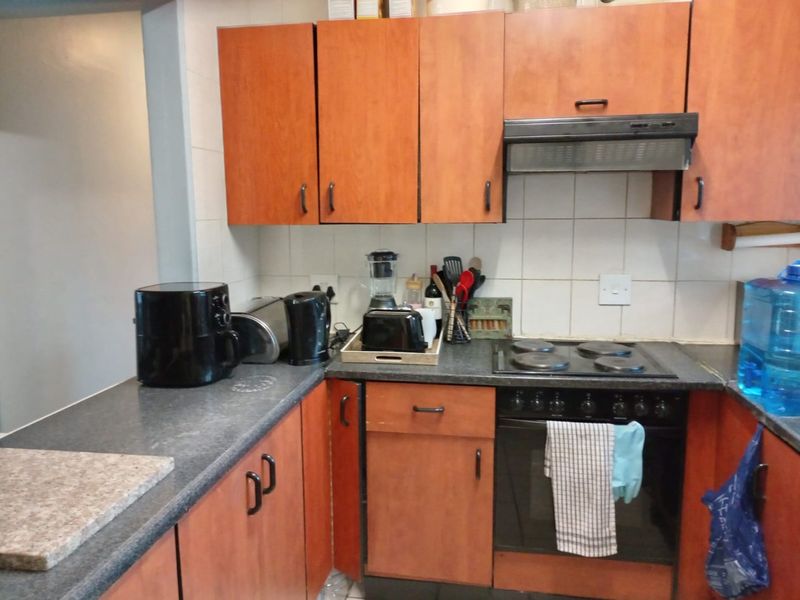 A functional kitchen featuring wood-look laminate cabinetry, dark countertops, a built-in oven with electric hob, and a tiled backsplash.