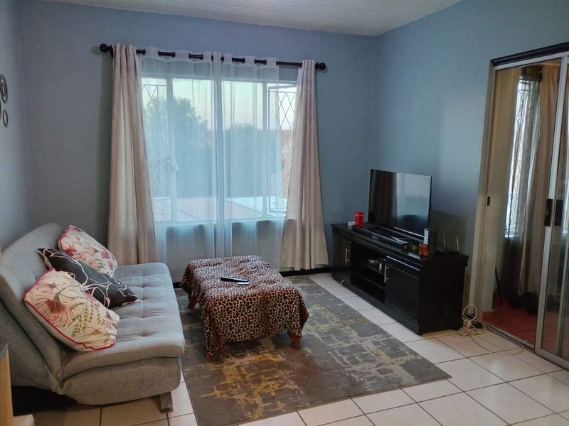 A living room featuring tiled flooring, a sliding glass door with security gate, and window security bars.