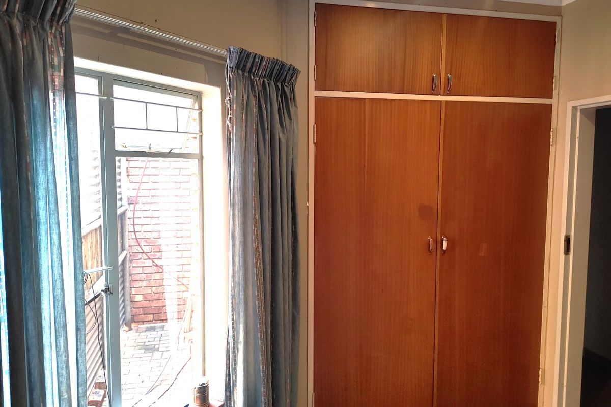 A bedroom featuring a full-height built-in wooden wardrobe and a metal-framed window overlooking an exterior brick area.