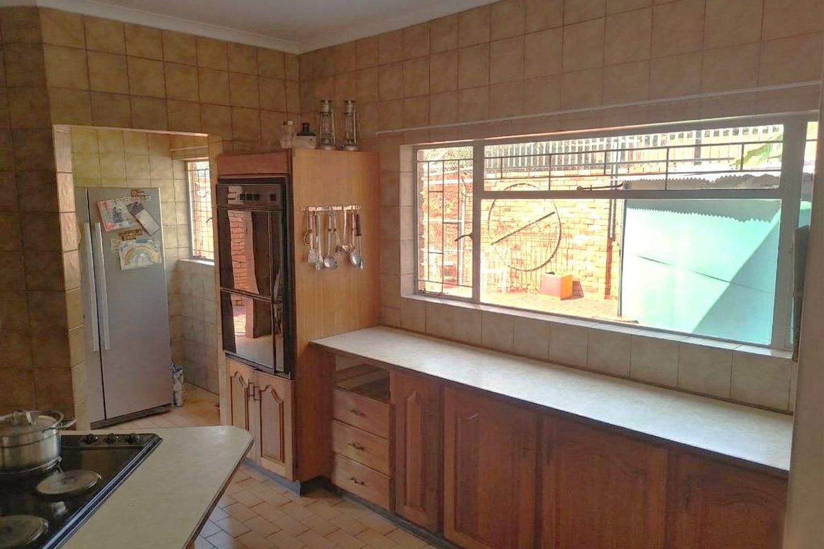 A functional kitchen featuring wooden cabinetry, laminate countertops, built-in oven, and hob, with tiled walls and flooring throughout.