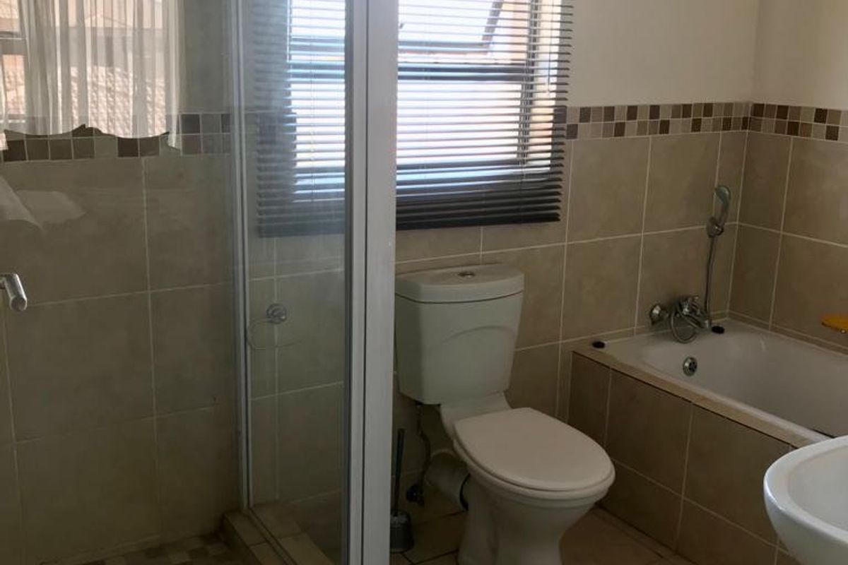 A functional bathroom featuring a separate shower enclosure, a bathtub, a toilet, and neutral wall and floor tiling.