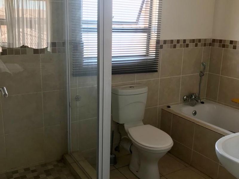 A functional bathroom featuring a separate shower enclosure, a bathtub, a toilet, and neutral wall and floor tiling.