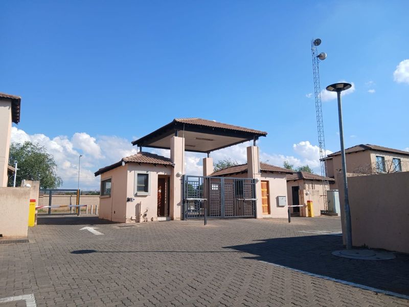 The entrance to the townhouse complex features a secure guard house, automated boom gates, and paved driveway access.