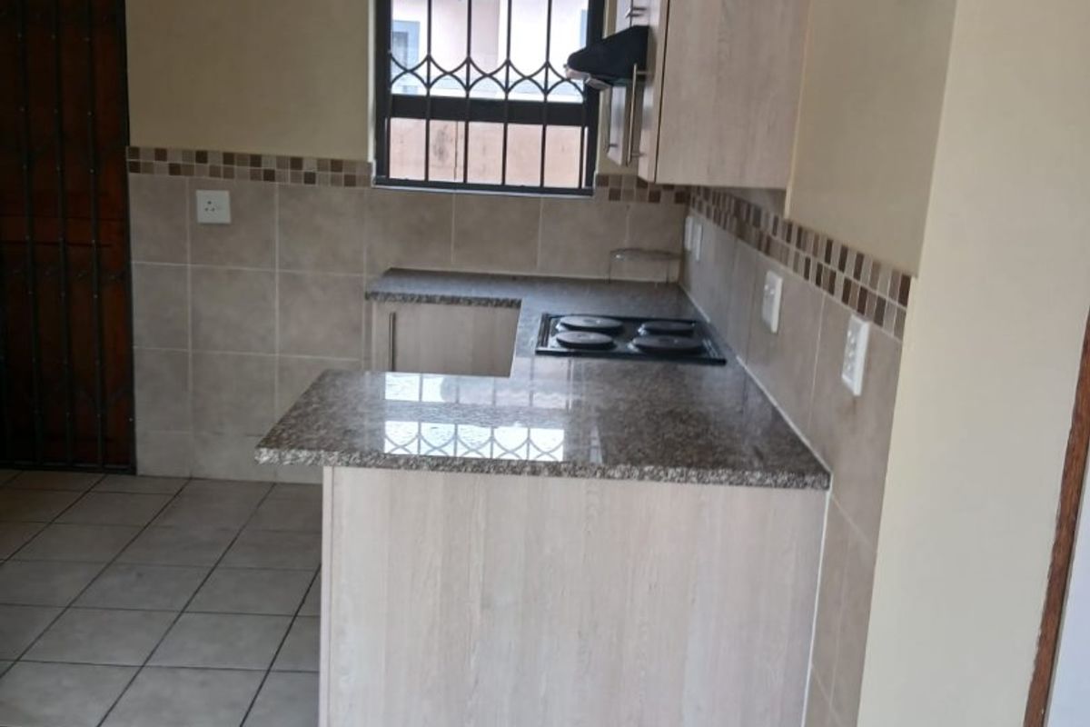 A functional kitchen featuring granite countertops, built-in cabinetry, an electric hob, and tiled flooring with security features on the window and door.