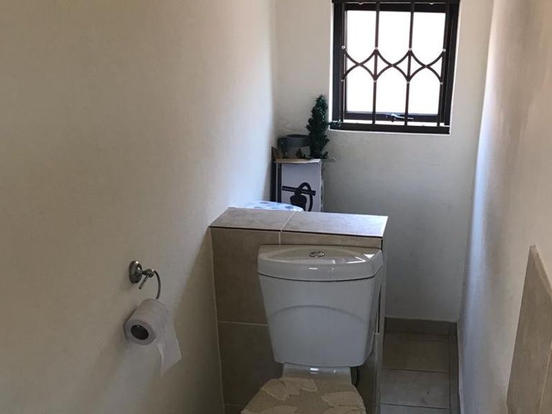 A compact bathroom featuring a toilet, bidet, and tiled flooring with a window fitted with security bars.
