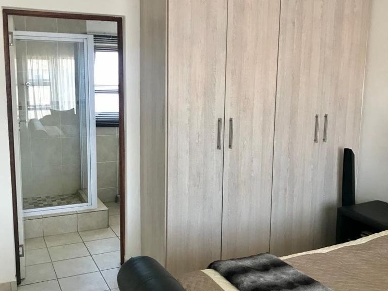 A bedroom featuring light wood-finish built-in cupboards, tiled flooring, and direct access to an en-suite bathroom with a shower.