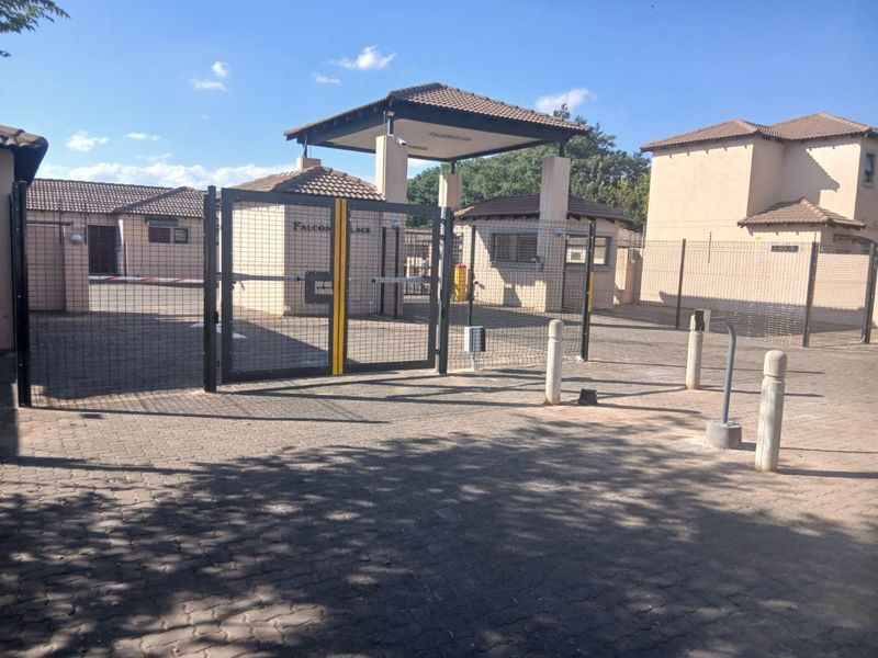 Secure gated entrance to the townhouse complex featuring a guard house, paved driveway, and perimeter fencing.