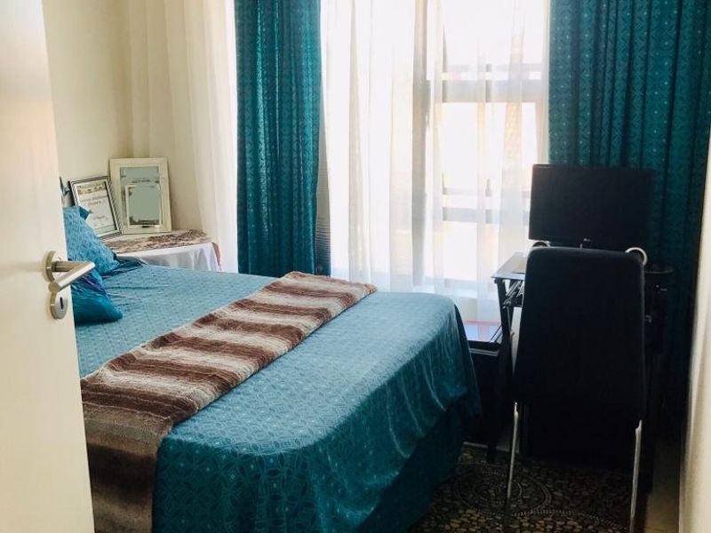 A compact bedroom featuring tiled flooring and a large window with floor-to-ceiling curtains, providing natural light to the space.