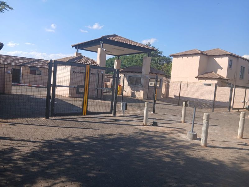 Secure gated entrance to the townhouse complex featuring a guard house, paved driveway, and perimeter fencing.