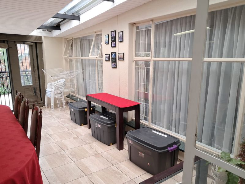 A covered patio area featuring tiled flooring, large windows with security bars, and a translucent roof section providing natural light.