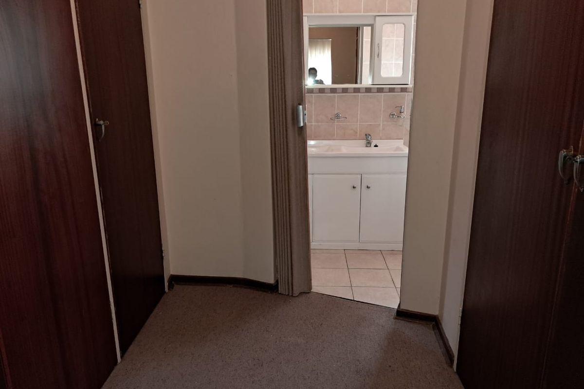 A view from a carpeted hallway into a bathroom featuring a built-in vanity, tiled splashback, and wall-mounted mirror.