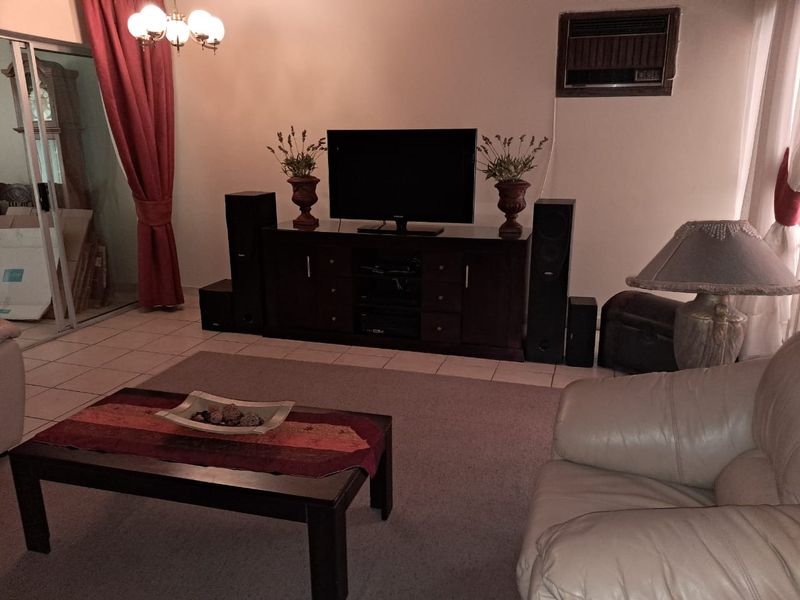A living room featuring tiled flooring, a window-mounted air conditioning unit, and access to an outdoor area via a sliding glass door.