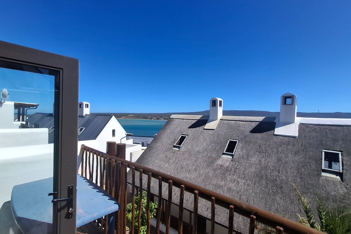 A scenic elevated view overlooking neighbouring thatched-roof properties with a clear blue sky and distant water horizon.