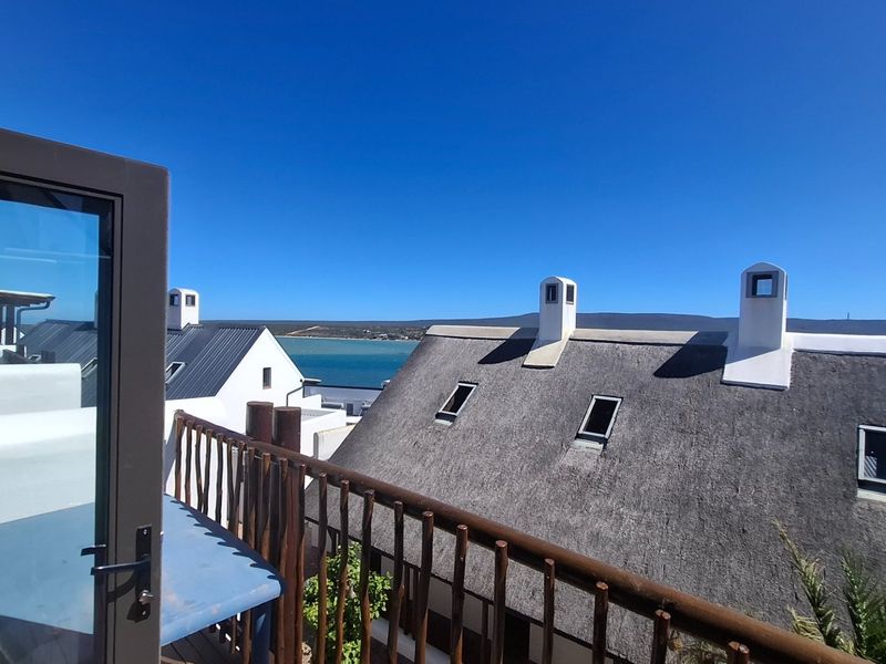 A scenic elevated view overlooking neighbouring thatched-roof properties with a clear blue sky and distant water horizon.
