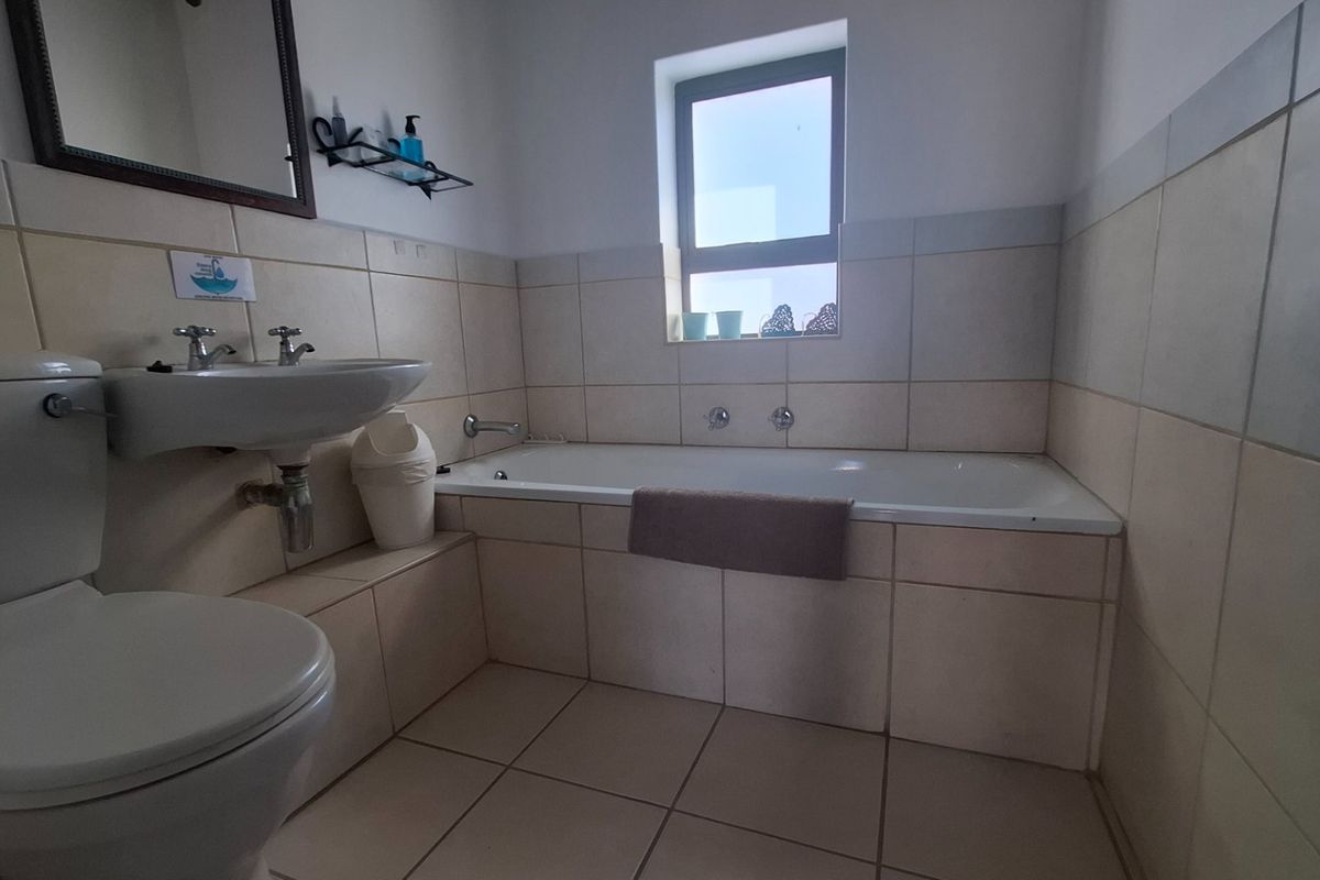 A functional bathroom featuring a bathtub, pedestal basin, and toilet with neutral wall and floor tiling.