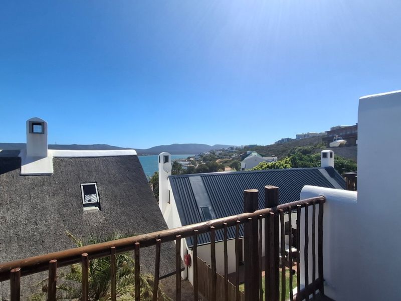 A balcony with a timber railing offering a scenic view of the surrounding coastal neighborhood and distant hills.