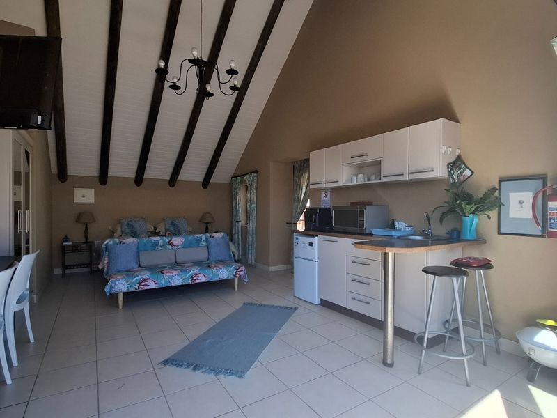 Open-plan studio apartment featuring a kitchenette, tiled flooring, and a vaulted ceiling with exposed timber beams.