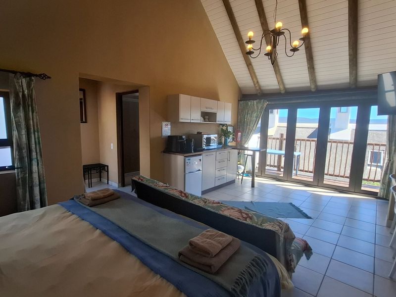 Open-plan studio apartment featuring a kitchenette, vaulted ceilings with exposed timber beams, tiled floors, and direct access to a private balcony.