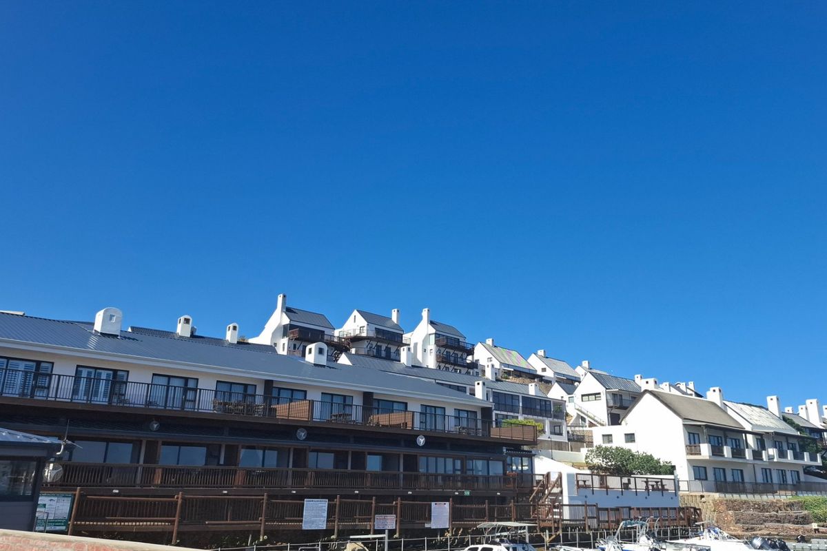 A view of a multi-level apartment complex featuring white facades, metal roofing, and timber-railed balconies overlooking a waterfront area.