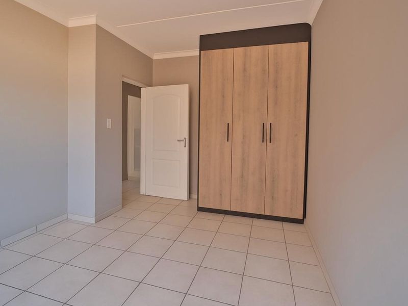 A clean, empty bedroom featuring neutral wall tones, light-colored floor tiles, and a modern built-in wardrobe with wood-grain finish.