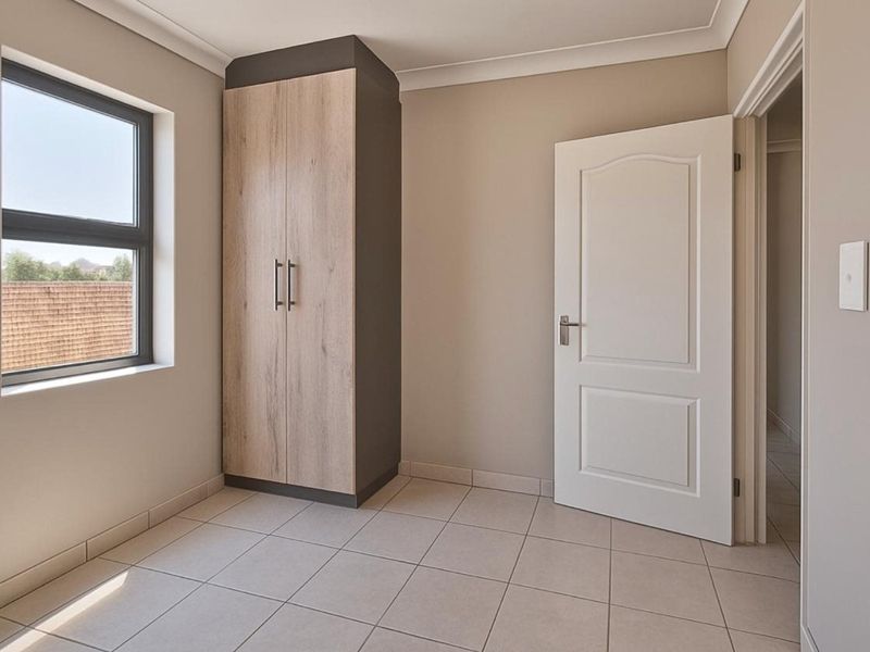 A clean, empty bedroom featuring neutral tiled flooring, a modern built-in wardrobe, and natural light from the window.
