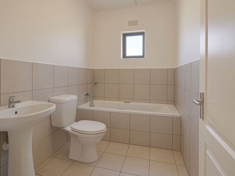 A clean, neutral-toned bathroom featuring a pedestal basin, a standard toilet, and a built-in bathtub with tiled surrounds.