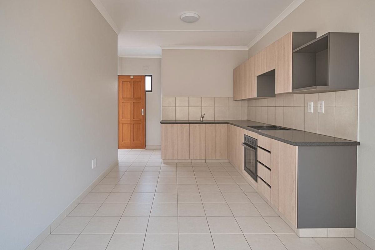 A clean, modern kitchen featuring light wood-tone cabinetry, dark countertops, built-in oven and hob, tiled backsplash, and neutral floor tiles.