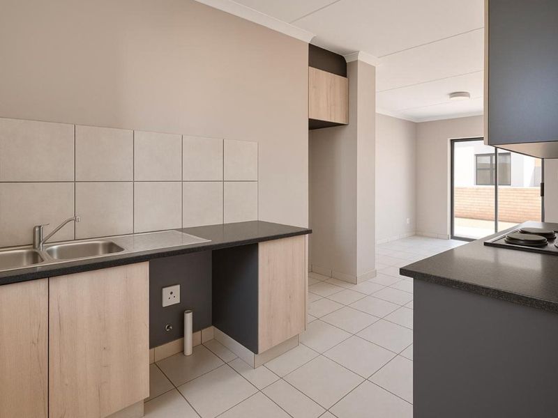 Modern open-plan kitchen featuring light wood-tone cabinetry, dark countertops, ceramic tile flooring, and direct access to an outdoor patio area.
