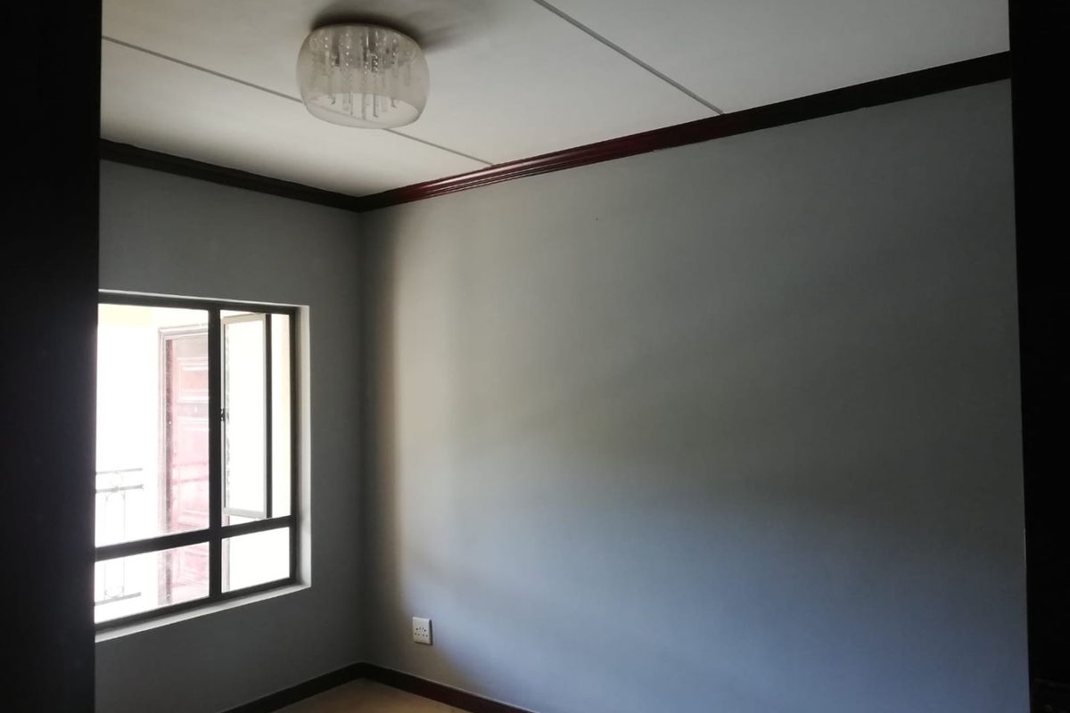 An empty bedroom featuring grey walls, dark trim, a ceiling light fixture, and a window providing natural light.