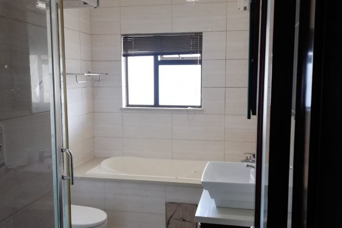 A functional bathroom featuring a built-in bathtub, glass shower enclosure, vessel sink with vanity, and neutral wall and floor tiling.