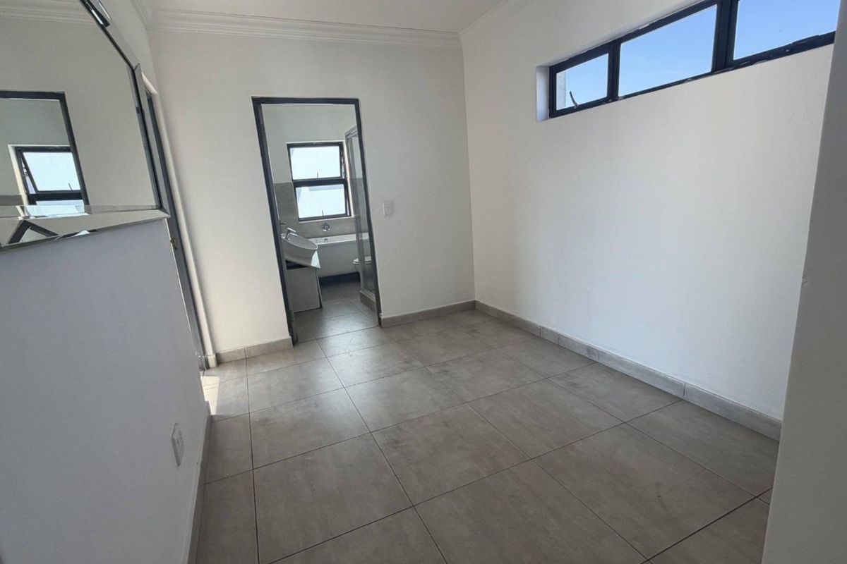 A bright, empty bedroom featuring neutral tiled flooring, high-level windows, and direct access to an en-suite bathroom.