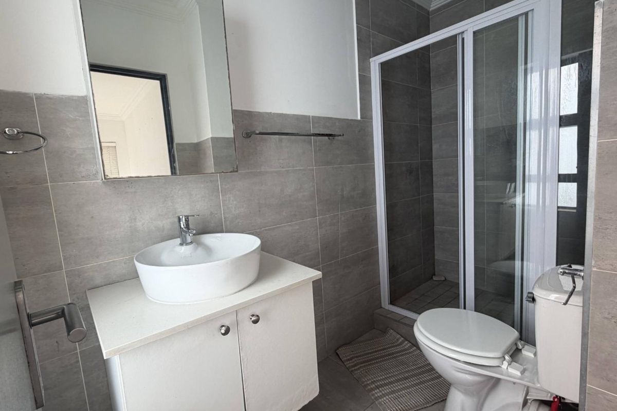A modern bathroom featuring a vessel sink vanity, a glass-enclosed shower, and neutral grey wall tiling.
