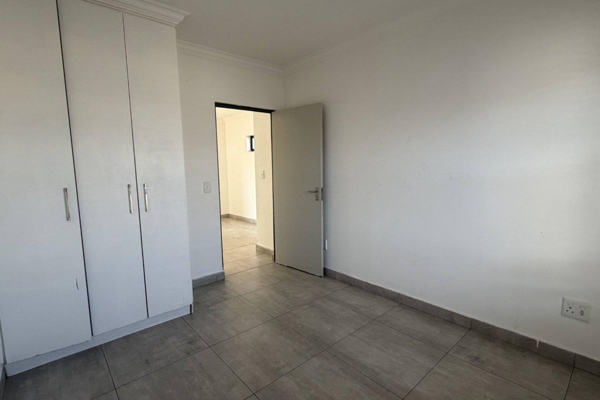 A clean, empty bedroom featuring neutral tiled flooring and built-in cupboards, offering a blank canvas for personalization.