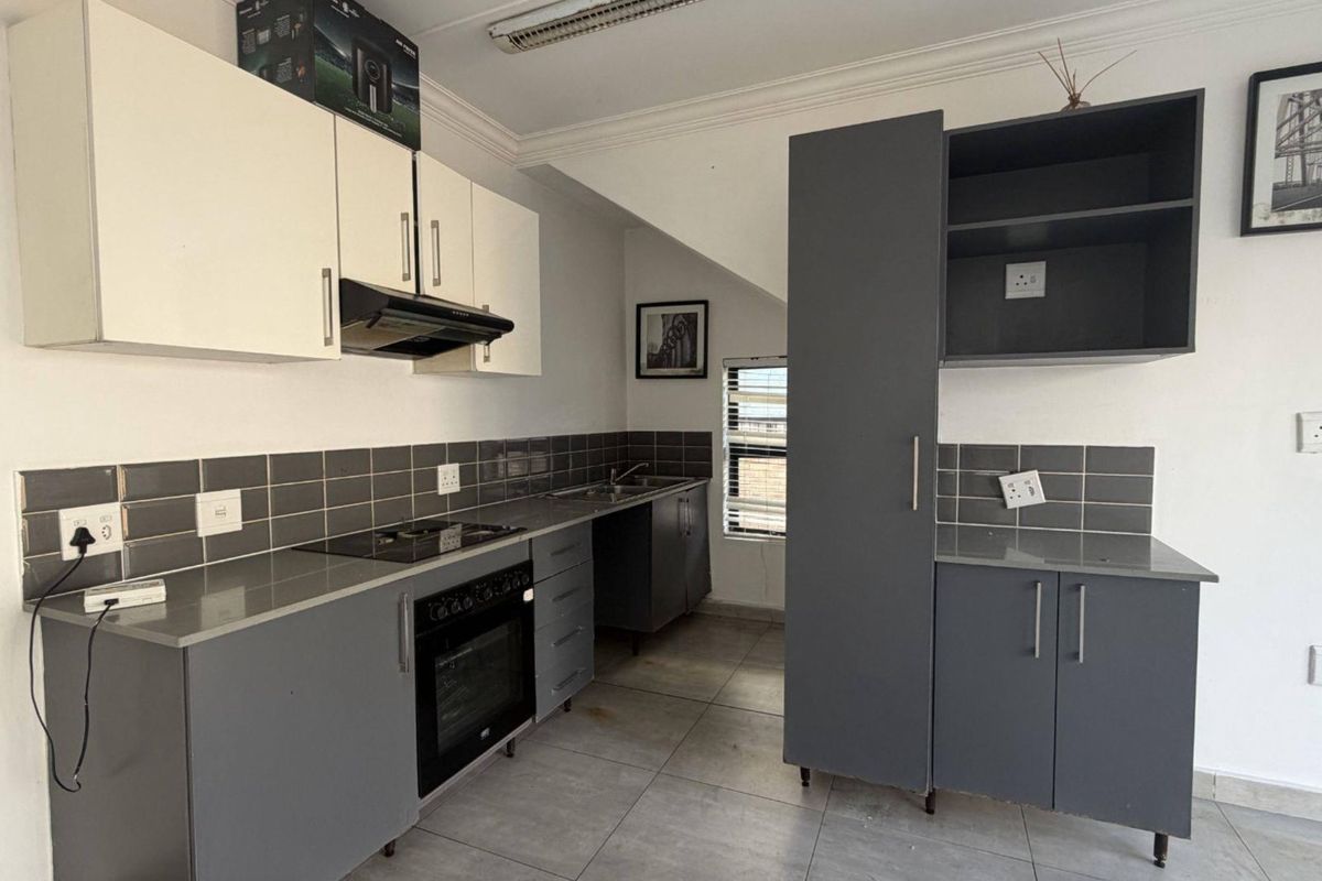 A modern, functional kitchen featuring grey cabinetry, stone countertops, a tiled backsplash, and integrated appliances including an oven and hob.