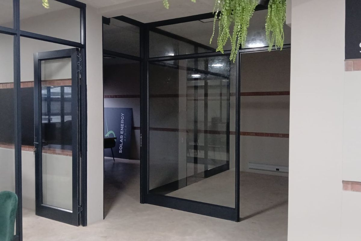 Modern commercial office space featuring glass partition walls, black aluminium framing, and an exposed brick accent wall, providing a professional and open work environment.