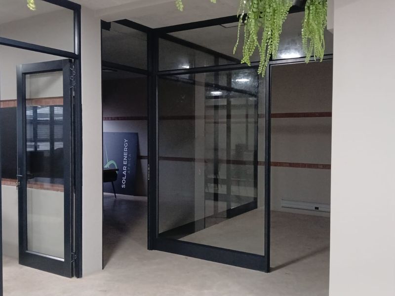 Modern commercial office space featuring glass partition walls, black aluminium framing, and an exposed brick accent wall, providing a professional and open work environment.