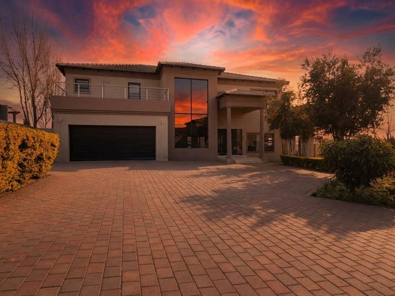 A modern double-story residence featuring a paved driveway, double garage, and an upper-level balcony, set against a vibrant sunset sky.