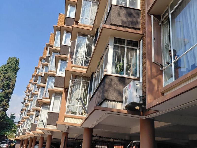 Exterior view of an apartment building featuring a covered ground-level parking area, brick facade, and multiple levels of casement windows.
