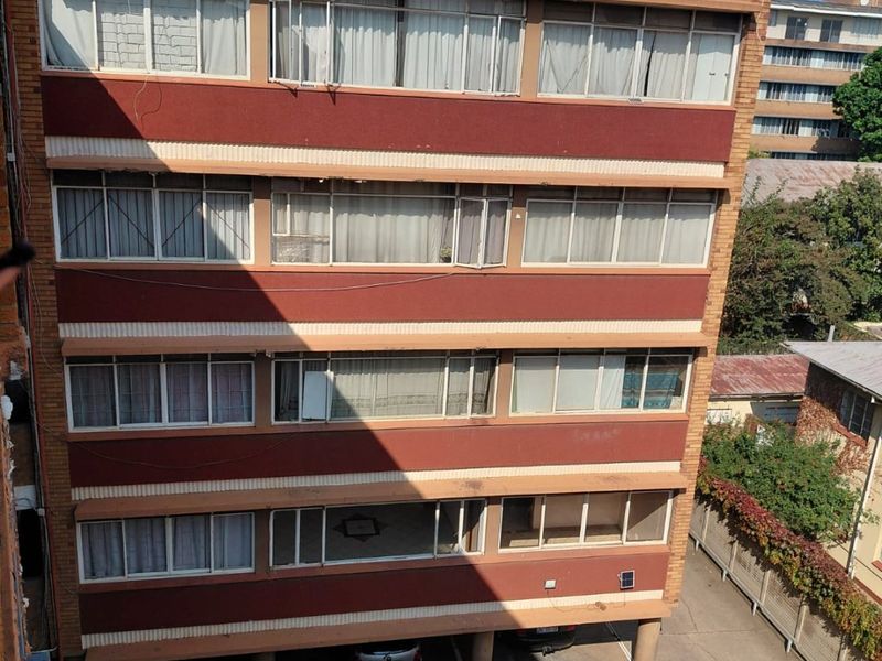 Rear elevation of a multi-story apartment building featuring brick facade, concrete support pillars, and a paved ground-level parking area.