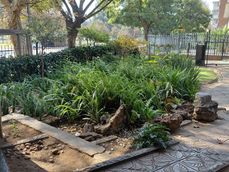 A covered patio area featuring decorative leaf-patterned stone paving and a landscaped garden bed with established greenery and rock features.