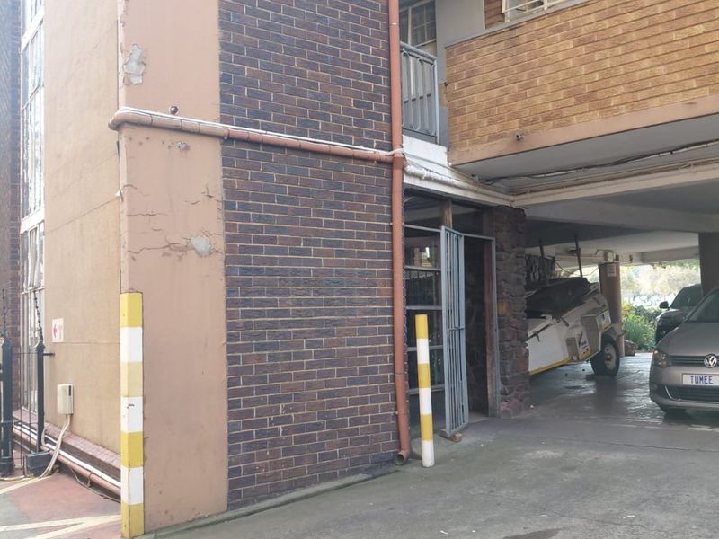 Exterior view of an apartment building facade showing a covered parking area, brickwork, and concrete driveway with visible signs of exterior wear.