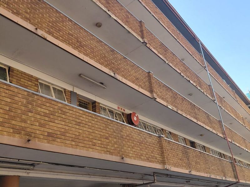 Exterior view of a multi-story apartment building featuring a brick facade, open-plan covered parking area, and balcony access for upper levels.