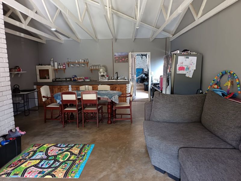 Open-plan living and kitchen area featuring exposed roof trusses, concrete flooring, and a rustic brick-based kitchen counter.
