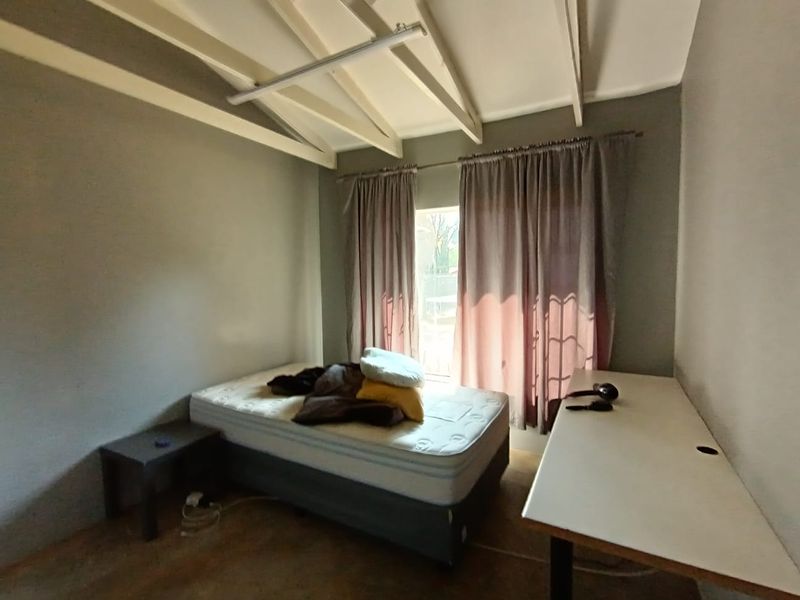 A bedroom featuring a vaulted ceiling with exposed rafters and natural light through a window with curtains.