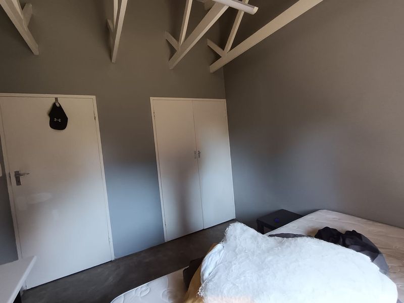 Bedroom featuring exposed white roof trusses, grey walls, concrete flooring, and built-in cupboard storage.
