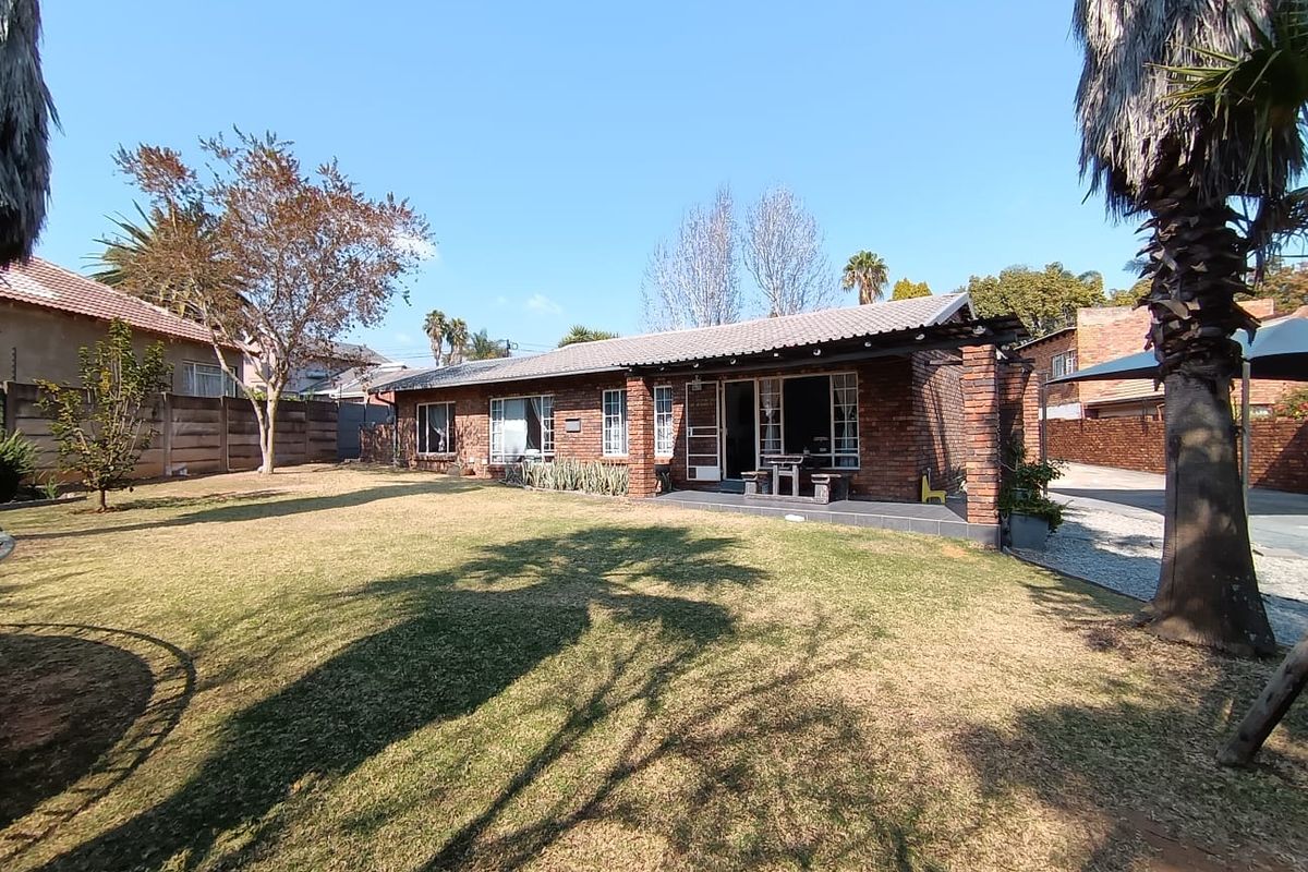 Rear view of a single-story brick house featuring a covered patio area, a spacious lawn, and established garden surroundings.